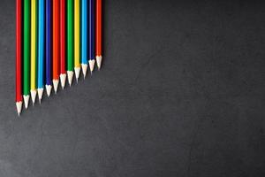 Pencils of different colors in a row on a black textured background. photo