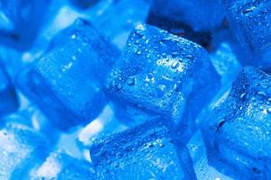 Ice cubes with water drops scattered on a blue background, top view. photo