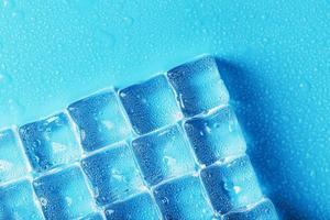 Ice made of cubes lined up with drops on a blue background with free space photo