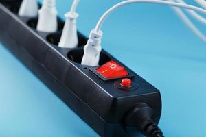 Black surge protector with a red button and connected white wires of electrical appliances on a blue background. photo