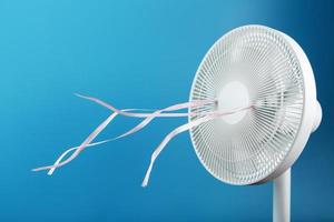 The electric fan is white with pink ribbons fluttering in the wind on a blue background photo