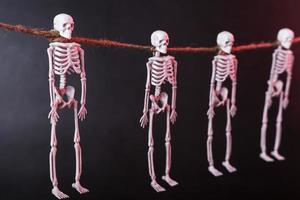 Four skeletons suspended by the neck on a rope with silhouettes on a dark background photo