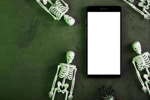los esqueletos decorativos se encuentran cerca del teléfono inteligente en un fondo oscuro. foto