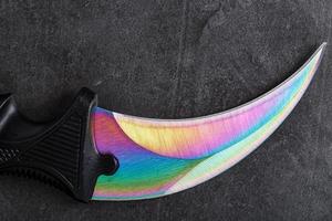 The curved sharp blade of the Kerambit Dagger is a gradient rainbow color on a dark background. photo