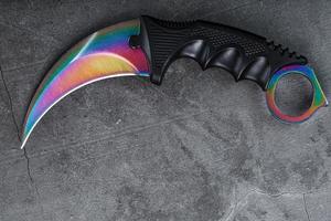 Kerambit dagger with a rainbow-colored blade on a dark textured background. photo