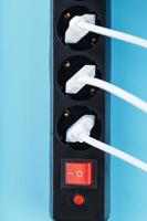 A black mains filter with electrical outlets inserted into it with white plugs of electrical appliances on a blue background photo