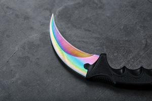 Kerambit dagger with a rainbow-colored blade on a dark textured background. photo