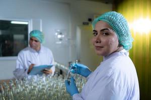 El oficial de control de calidad del producto en la línea de producción de jugo de frutas realiza una inspección de las botellas utilizadas para contener jugos de frutas. foto