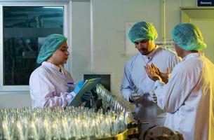 El oficial de control de calidad del producto en la línea de producción de jugo de frutas realiza una inspección de las botellas utilizadas para contener jugos de frutas. foto