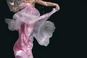 young beautiful woman in long  pink dress with cage in her hands underwater photo