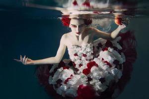 Woman in dress made of white and red roses underwater. Fairy tale, art, fashion concept photo