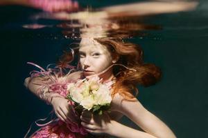 Young redhead girl in dress made of roses underwater photo