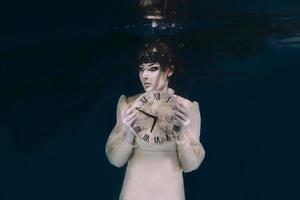mujer espeluznante con reloj en sus manos en velo negro bajo el agua foto
