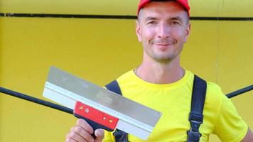 portrait d'un maître de réparation et de construction de maison avec un outil de gros plan. un constructeur avec une spatule à l'extérieur de la maison. travaux de plâtrage et de finition, services de peintre, réparation de la façade video