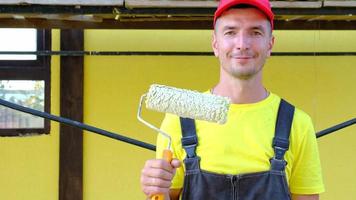 Portrait of a house repair and construction master with a close-up tool. A builder with a paint roller in the exterior of the house. Finishing works, painter's services, repair of the facade video