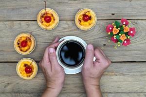 hand holding coffee cup with egg tart on wood table,top view photo