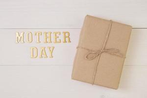 Gift box and text is mother day on wooden background with romantic, presents word and message pastel tone, package with congratulation with happy, spring or summer nature on desk, holiday concept. photo