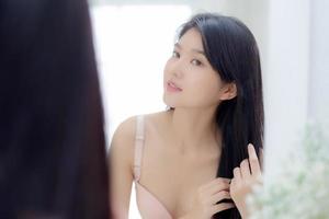 Beautiful young asian woman smiling look at mirror of touch hair in the room, cosmetic for hygiene hair care, beauty asia girl happy for hairstyle treatment at home, lifestyle and makeup concept. photo