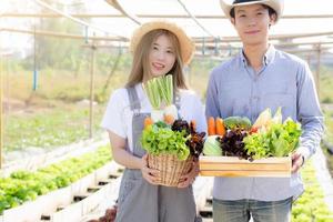 hermoso retrato joven mujer y hombre asiáticos cosechan y recogen huertas orgánicas frescas en una canasta en la granja hidropónica, agricultura para alimentos saludables y concepto de empresario empresarial. foto