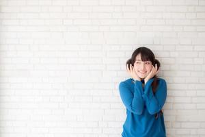 retrato de una hermosa joven asiática disfrutando y feliz de pie sobre un fondo de ladrillo de pared gris con textura de cemento, la chica es una sonriente y alegre sobre hormigón. foto