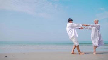 pareja de jubilados asiáticos relajándose junto al mar en verano. una anciana bailando con su pareja en la playa. foto