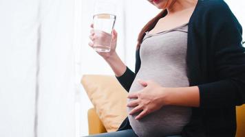 Asian pregnant woman drinking water on the sofa at home. photo