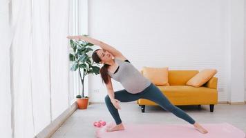 hermosa joven asiática embarazada en ropa deportiva está haciendo yoga en casa. foto