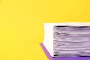 Close up of a pile of unfinished documents awaiting verification on a yellow background. Business and education concept. Copy space photo