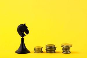 Black chess piece of a horse, with coins in the form of steps on a yellow background. Business concept. Game, strategy, wisdom, determination. Copy space. photo