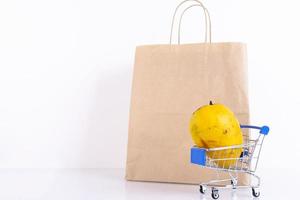 Yellow mango, a favorite Thai fruit in a shopping cart, and a craft paper bag on a white background. ECO, environmentally friendly product. Copy space. photo