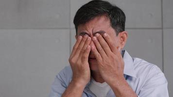 un anciano asiático se frotaba los ojos, cansado de mirar durante mucho tiempo. foto