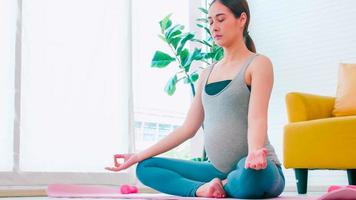 hermosa joven asiática embarazada en ropa deportiva está haciendo yoga en casa. foto