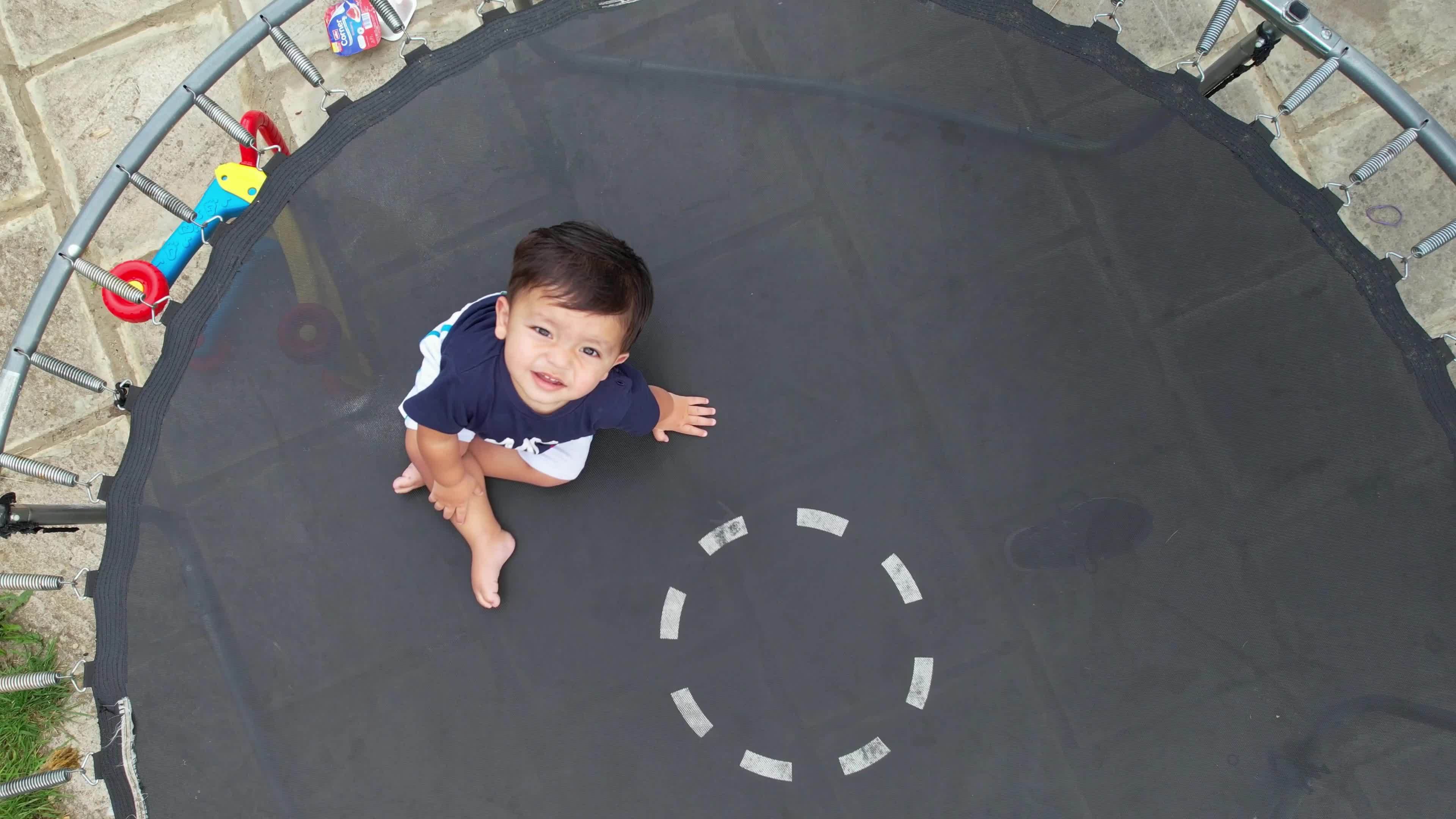 1 Year Old Baby Boy is posing under the drone's camera on a trampoline