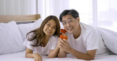 feliz pareja asiática sosteniendo decoraciones de corazón rojo juntas en un dormitorio. foto