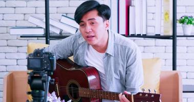 A young Asian man is playing the guitar and singing on social media by streaming live from his home. photo