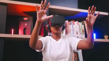 A schoolgirl sitting in front of library's bookshelf and using virtual reality glasses. photo