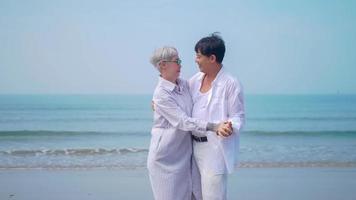 pareja de jubilados asiáticos relajándose junto al mar en verano. una anciana bailando con su pareja en la playa. foto