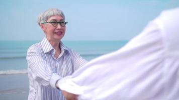 Asian retired couple relaxing by the sea in summer. A senior woman dancing with her partner on the beach. photo