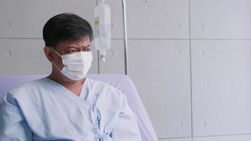 un anciano asiático está hospitalizado con covid-19. un anciano paciente que usa una máscara médica se sienta en la cama del paciente. foto