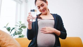 Asian pregnant woman drinking water on the sofa at home. photo