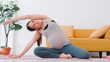 Beautiful young Asian pregnant woman in sportswear is doing yoga at home. photo