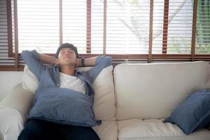 retrato joven apuesto hombre asiático tomando una siesta relajarse con acogedor en el sofá en casa, hombre de asia descansando y durmiendo el fin de semana con cansado y perezoso en el sofá en concepto de vacaciones, estilo de vida y bienestar. foto