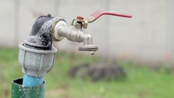 waterkraan op de achtergrond van de natuur. het openen of sluiten van een kraan om water te besparen duidt op een probleem met watertekort. rustieke fontein met daglicht. selectieve aandacht met onscherpe achtergrond. video