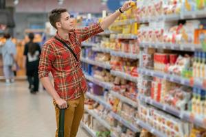 A young man in a plaid shirt buys groceries in a supermarket. A man takes goods from a shelf in a store photo