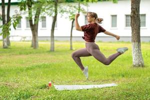 Young girl having online workout outdoors using laptop. Pilates or yoga video lesson on internet. Happy smiling girl practicing pilates lesson online in garden outdoors during quarantine. photo