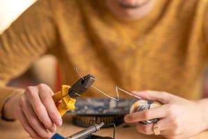 a young man solders a burnt-out microcircuit with a soldering iron photo