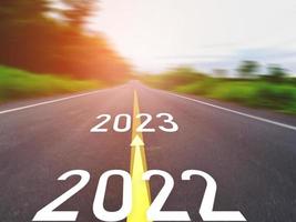 concepto de año nuevo y camino nuevo con flecha 2022 a 2023 escrito en la carretera asfaltada en un hermoso camino rural con campos de hierba verde en ambos lados concepto para el año nuevo o visión de 2023 foto