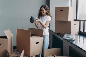 Happy girl unpacking cardboard boxes and taking the vase. European woman packing boxes to move. photo