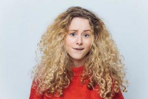 People, emotions and facial expressions concept. Adorable young woman being puzzled and surprised, isolated over white background. Curly young female in casual clothes exxpresses bewilderment photo