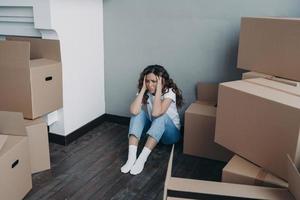 Anxious young lady is sitting on the floor going to relocate. Unhappy hispanic woman packing boxes. photo